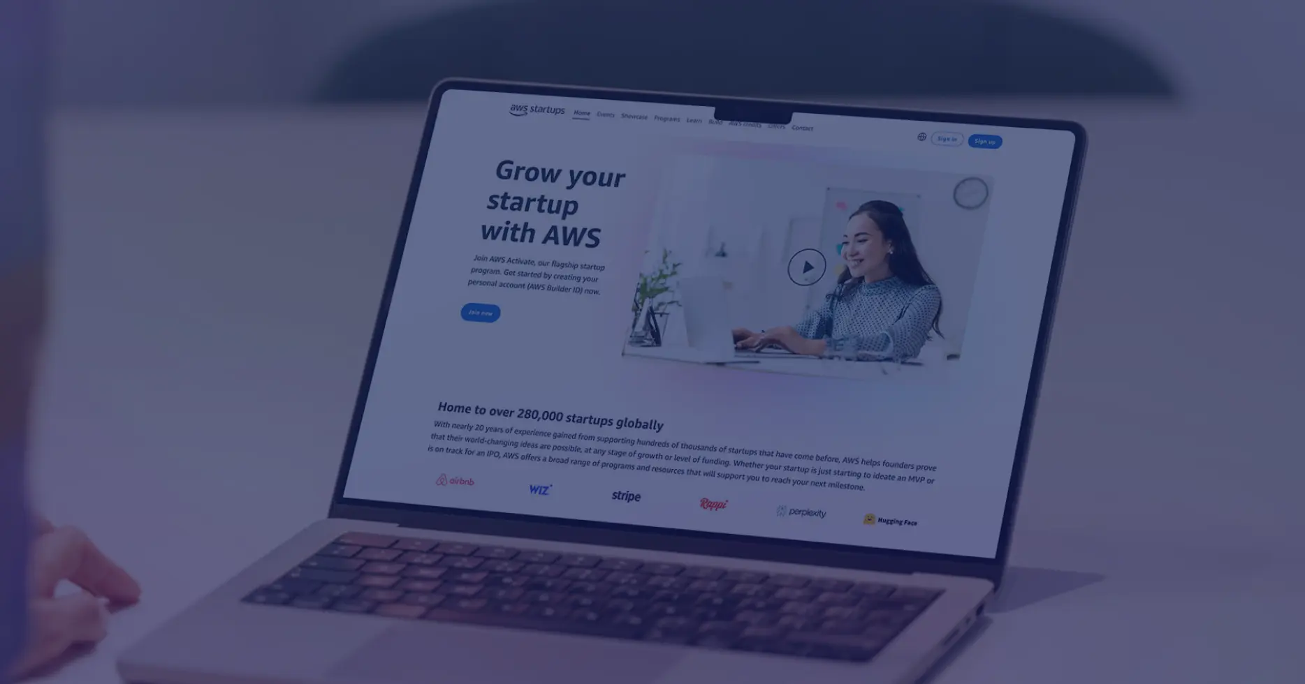 Close-up view of a laptop featuring AWS Activate homepage with headline “Grow your startup with AWS” and a video preview image of a businesswoman.