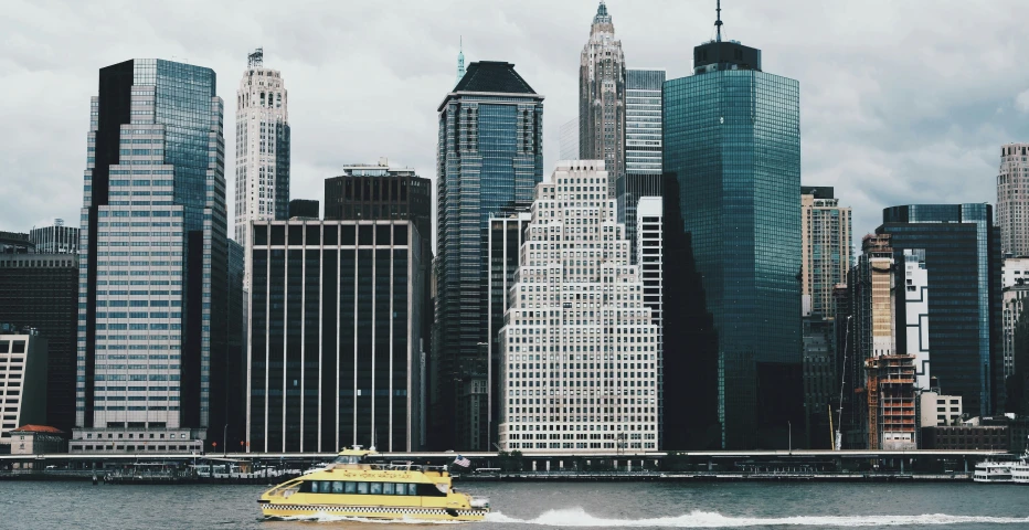 Manhattan skyline featuring modern glass skyscrapers with water taxi crossing New York harbor on overcast day.