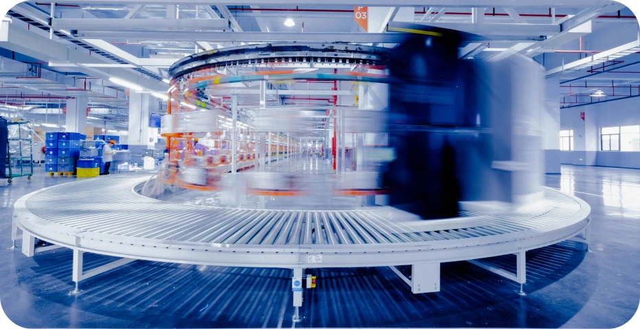 Automated distribution center with high-speed circular conveyor system showing motion-blurred packages moving through modern logistics warehouse facility.