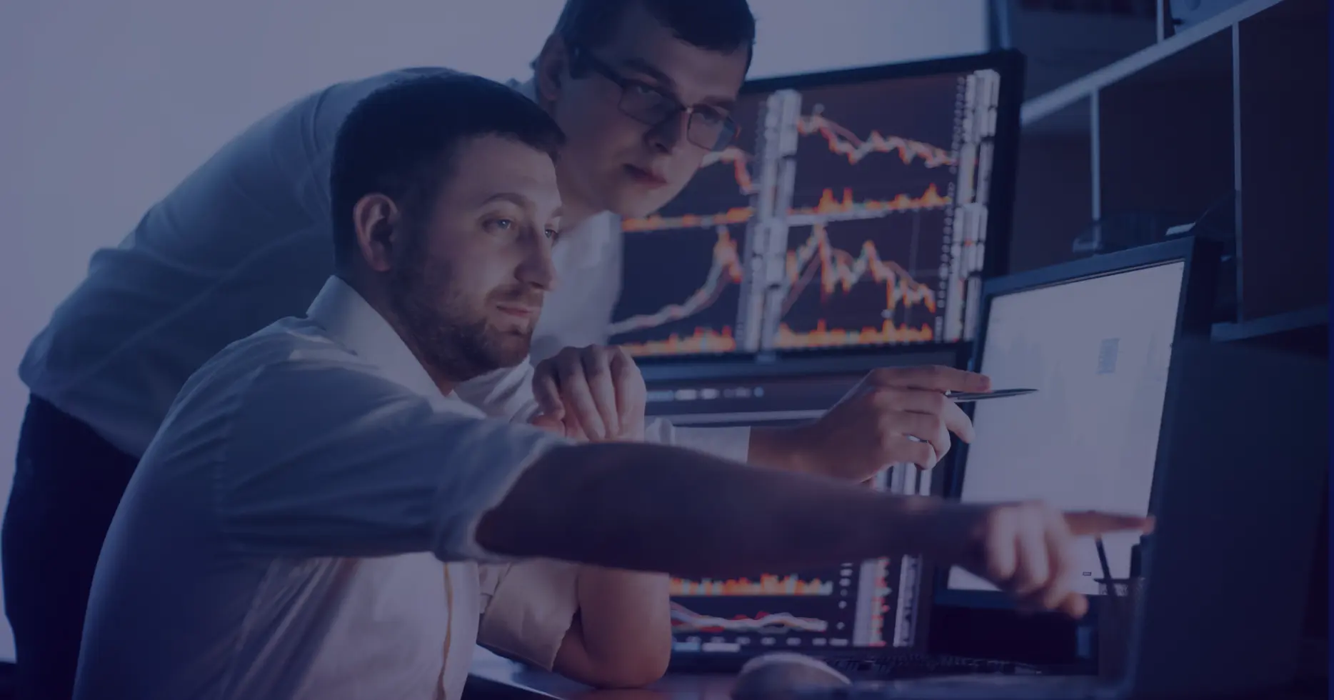 Team collaboration on financial data analysis, with one person pointing at a monitor displaying real-time stock market trends