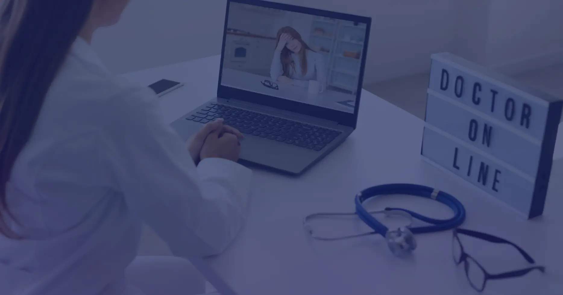 Healthcare professional conducting a virtual patient consultation via laptop with stethoscope and 'Doctor Online' signage – telehealth compliance setup