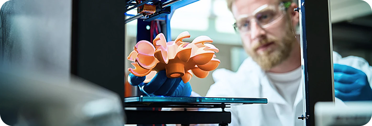 "A man wearing a robe is working on a 3D-printed model, adjusting details of the object he created with a 3D printer.